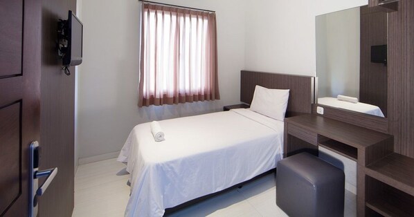 A hotel room with a bed, a desk, a chair, a mirror, and a window with curtains. - D'River Guesthouse (Bandung)
