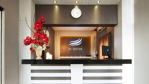 A reception desk with a clock, a floral arrangement, and a sign for 'D'RIVER Guest House'. - D'River Guesthouse (Bandung)