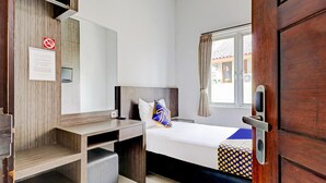 A hotel room with a bed, a desk, a chair, a window with curtains, and a door. - D'River Guesthouse (Bandung)