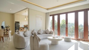 Una sala moderna con sofá, reposapiés y mesa de centro, un comedor con sillas y una cocina al fondo.