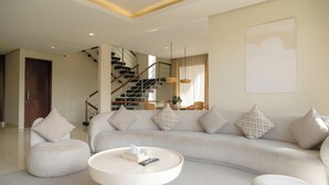 Una sala de estar moderna con sofá, reposapiés y una mesa de centro, una escalera y un comedor.