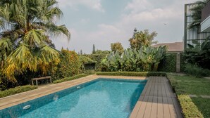 Piscina rectangular con muelle de madera, rodeada de abundante follaje y palmeras.