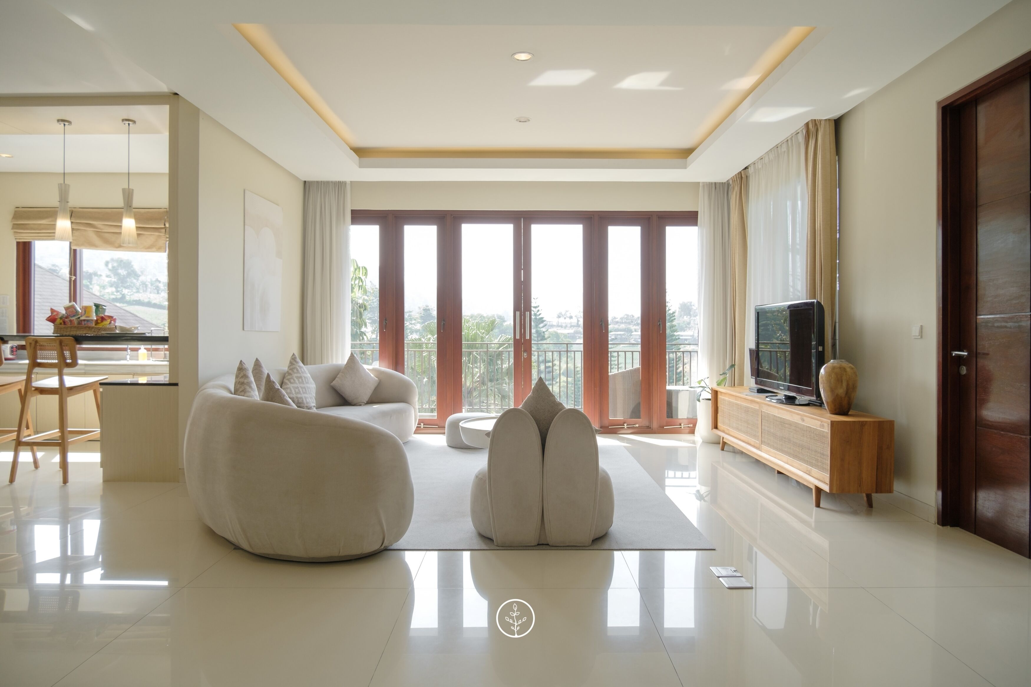 Una sala de estar moderna con sofá, reposapiés, mueble para TV y ventanas amplias.