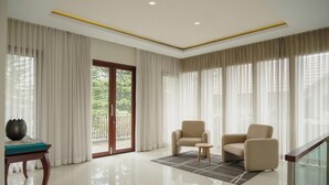 Un salón amplio con un gran ventanal corredera que da a un balcón, dos sillones color beige, una mesita redonda y un jarrón decorativo sobre una mesa de madera.