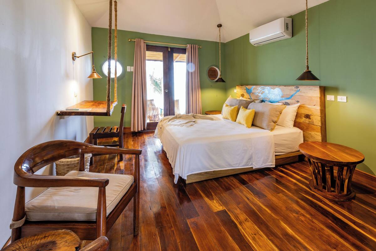 Een kamer met een bed, houten meubels, een hanglamp en uitzicht door een deur.