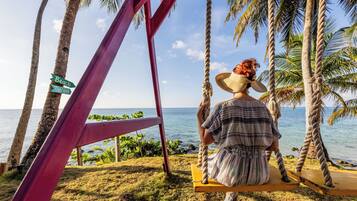 Relax on a swing overlooking the ocean, surrounded by palm trees.