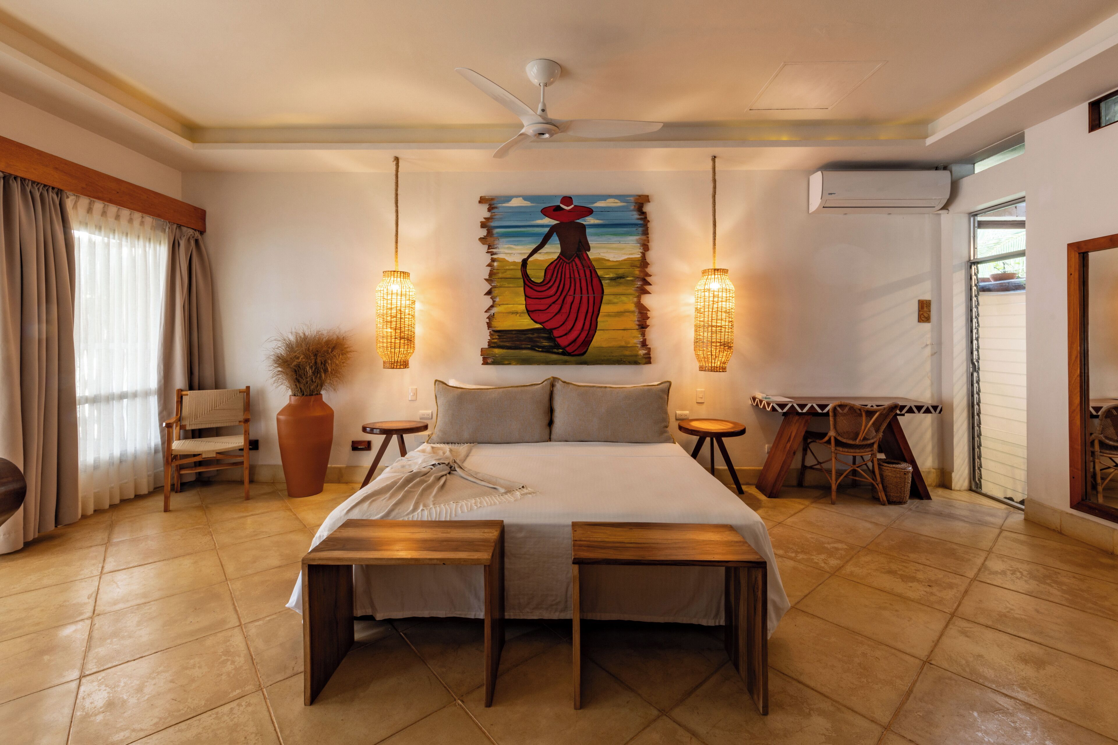 A bedroom with a bed, two bedside tables, a chair, a large vase, and a painting on the wall.