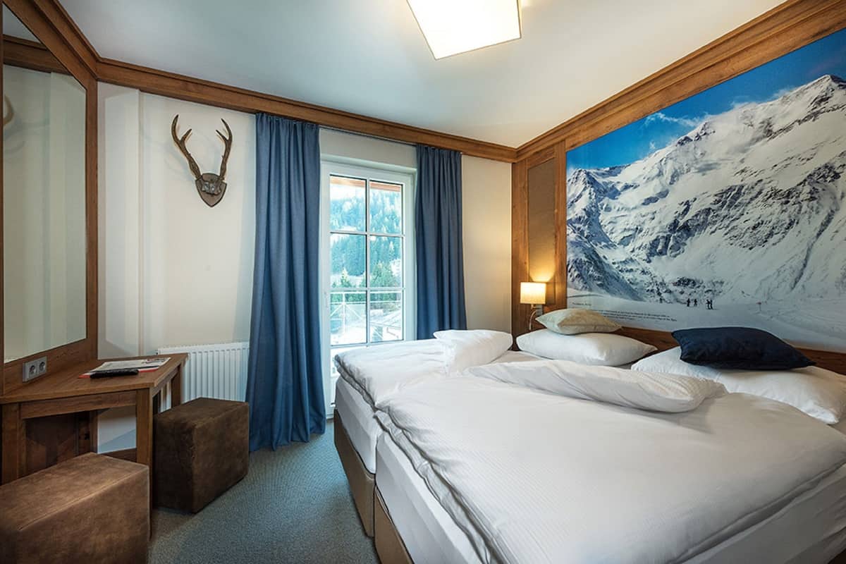 A hotel room with a bed, a desk, a chair, and a window with curtains.