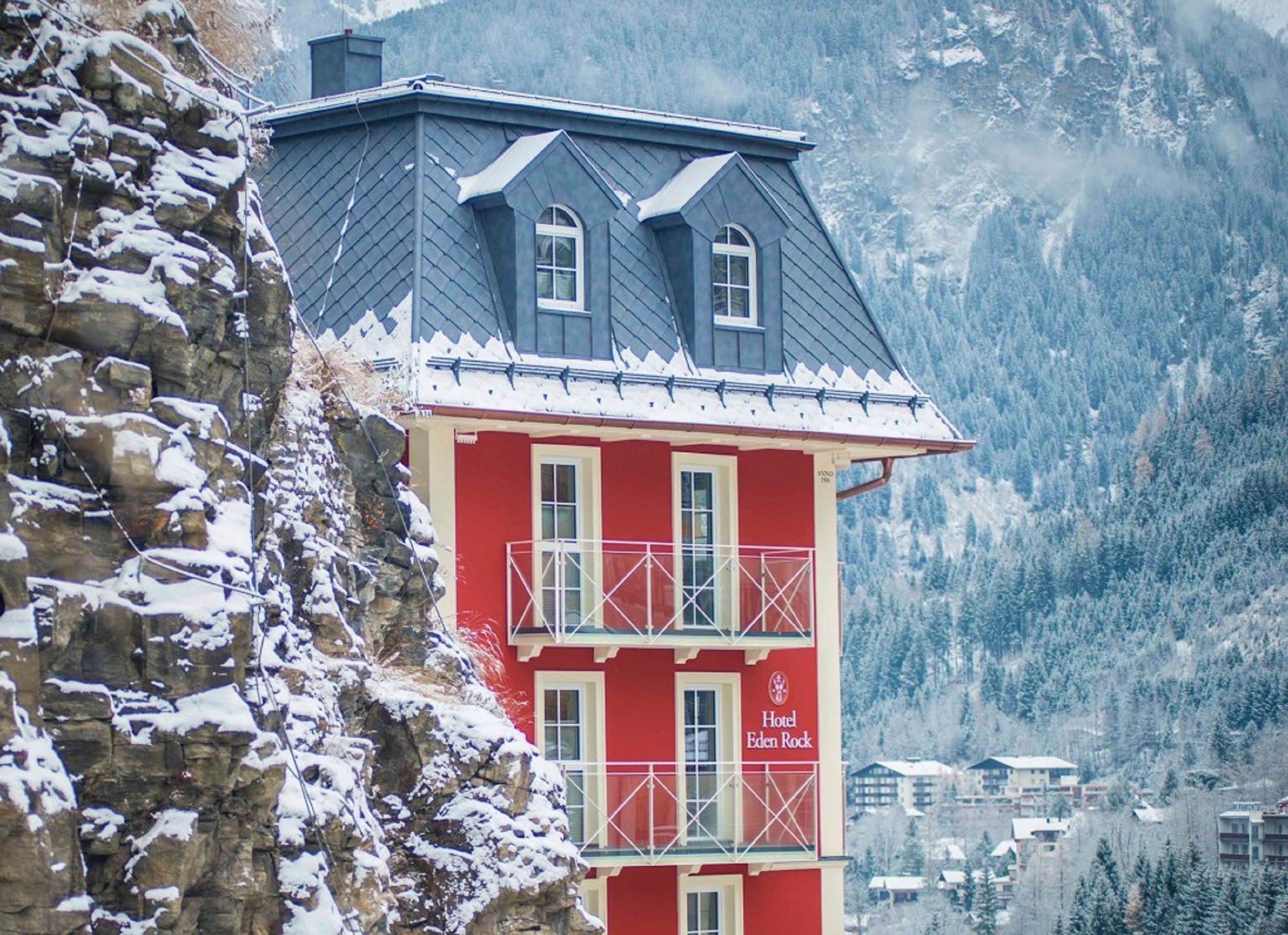 A red hotel with a balcony, set against a mountainous backdrop.