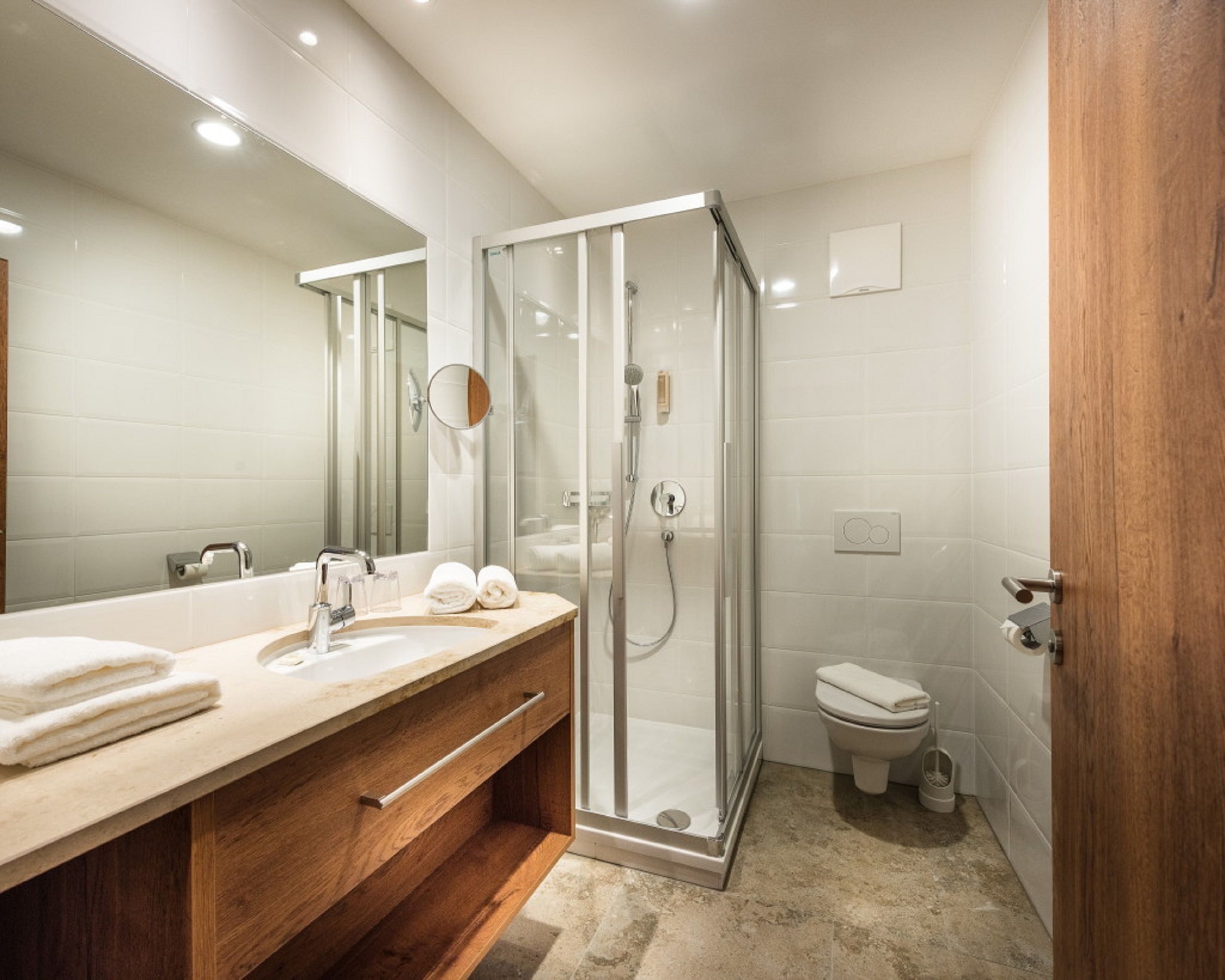 Un baño moderno con ducha envuelta en vidrio, tocador de madera con lavamanos y un inodoro.