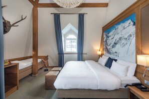Un dormitorio con una cama grande, cabecera de madera, cráneo de ciervo montado, pintura de montaña y una ventana con cortinas azules.