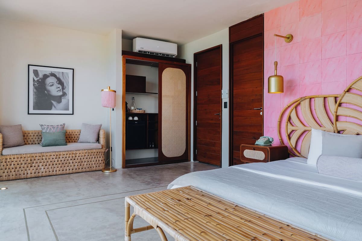 Ein Schlafzimmer mit einem Bett, einer Rattan-Couch, einem Kleiderschrank und einer rosa Wand.