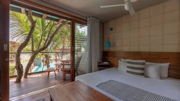 A bedroom with a wooden headboard, a bed with striped bedding, a nightstand, and a view of a pool and palm trees through a sliding glass door.