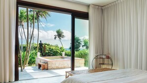 Une chambre dotée d’un grand lit, offrant une vue sur une piscine, et donnant sur un espace extérieur tropical agrémenté de palmiers.