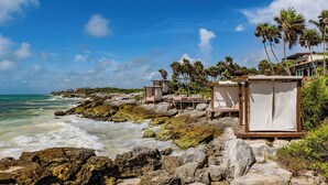 Une plage au paysage rocheux, bordée de palmiers, sous un ciel bleu et dégagé.