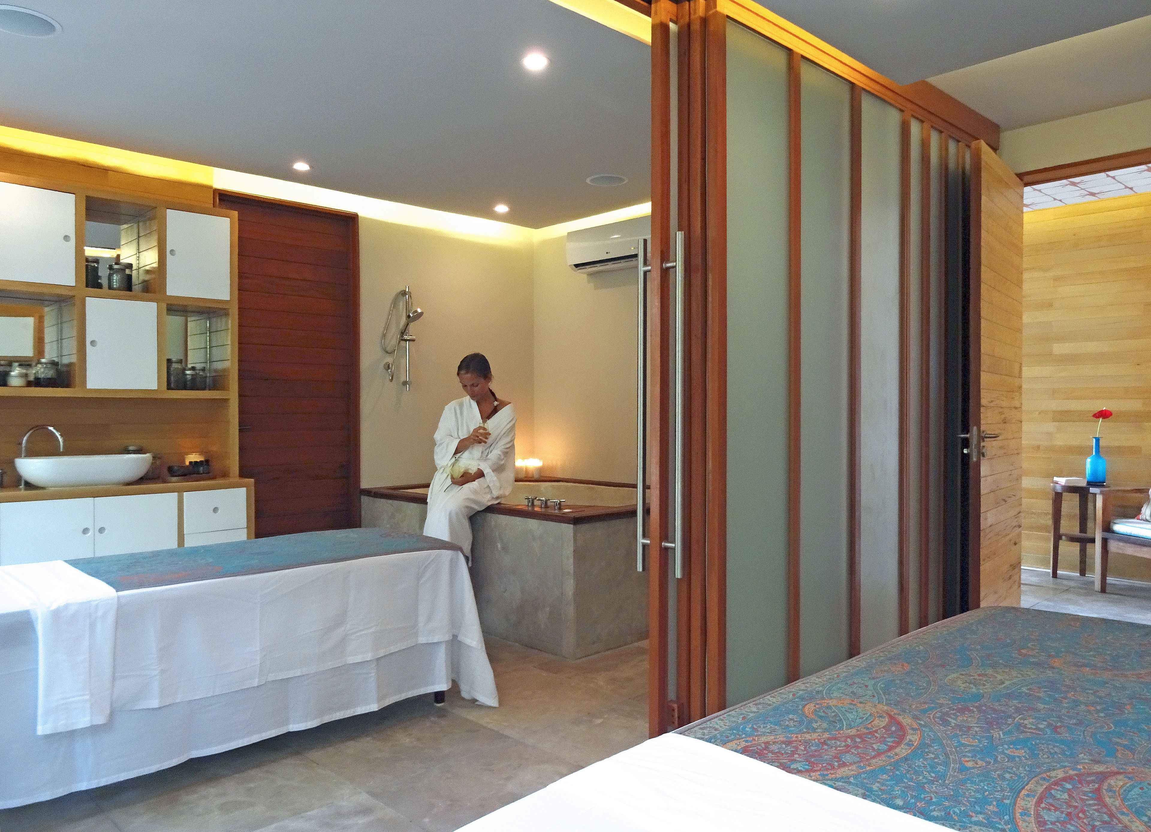 Habitación de hotel con cama, zona de estar, baño con ducha y una mesita con un florero.