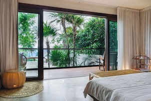 A room with a bed, a chair, a small table, and a view of greenery through a large glass door.