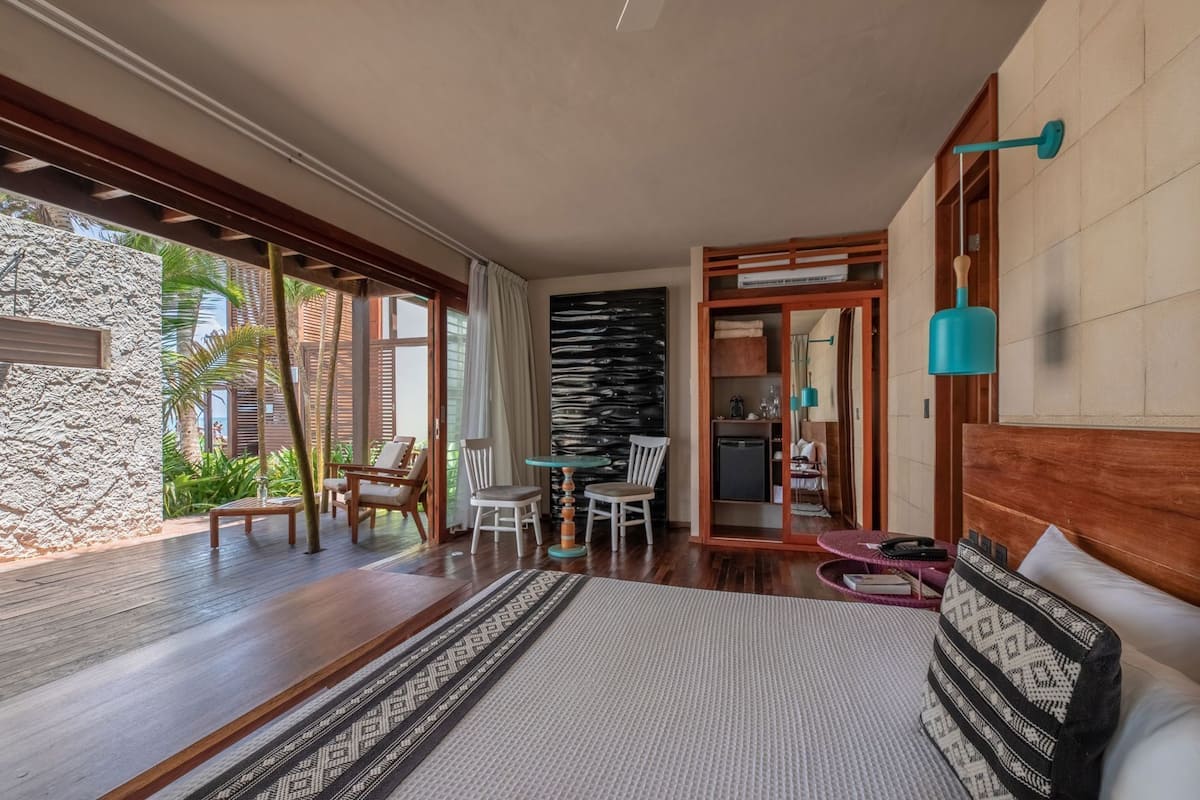 Ein Schlafzimmer mit einem großen Bett, einem Holztisch, Stühlen, einem kleinen Tisch und Blick ins Freie.
