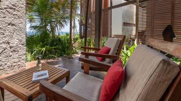 A wooden deck with a chair and table, surrounded by tropical plants and a stone wall.
