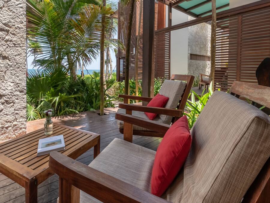 A wooden deck with a chair and table, surrounded by tropical plants and a stone wall.