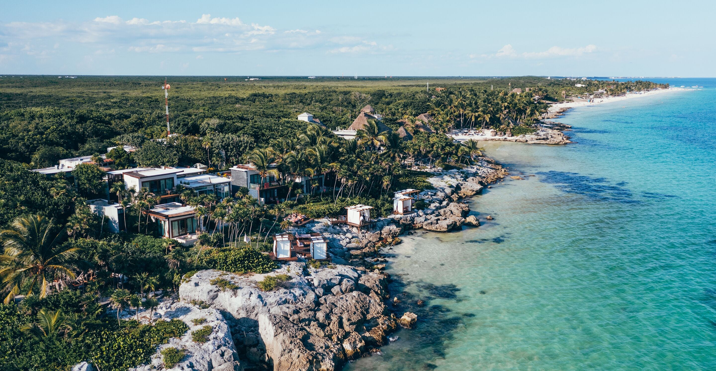 Vista aérea de un complejo turístico costero con varias edificaciones, una playa y densa vegetación tropical.