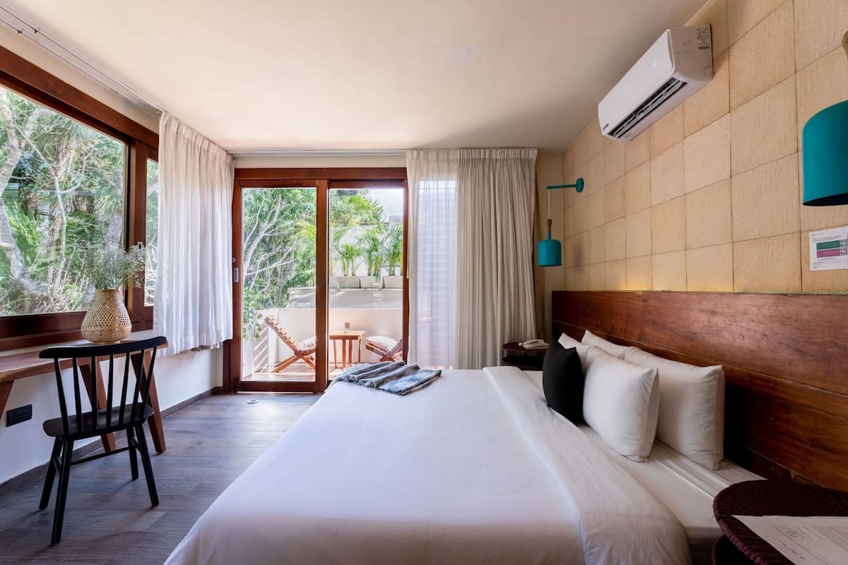 Ein Hotelzimmer mit Bett, Schreibtisch, Stuhl und einem Balkon mit Aussicht, sowie einer Klimaanlage.