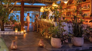 Un'area bar all'aperto con mobili in legno, piante in vaso e vista sul mare.