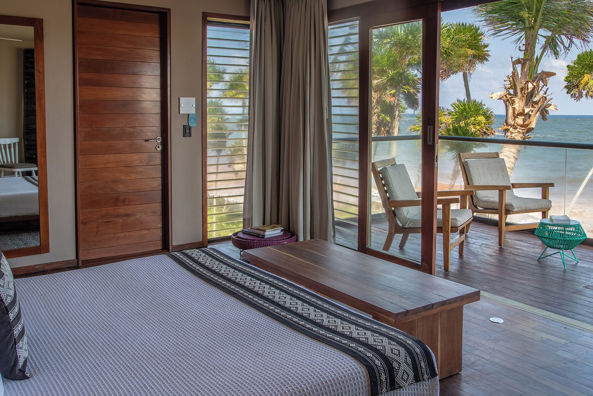 A bedroom with a large bed, a wooden nightstand, and a view of the ocean through floor-to-ceiling windows.