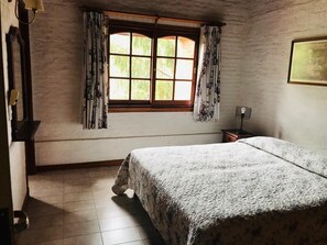 A bedroom with a bed, a window with curtains, a bedside table, and a wall-mounted lamp. - Vacances Dorado (Pinamar)