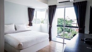 A hotel room with a large bed, a desk with a phone and remote, and a view of the city through the window. - Vanilla Residence Chiangmai (Chiang Mai)