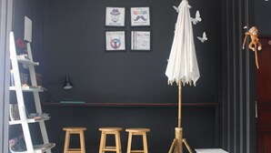 Una habitación con una pared oscura, una lámpara de pie blanca, una mesa blanca y una estantería blanca con libros.