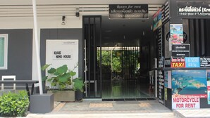 Entrada de un hotel con un cartel que indica Krabi Nemo House, un letrero de alquiler de motocicletas y un letrero de taxi.