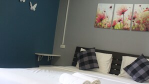 Una cama bien tendida con sábanas blancas, un cabecero con almohadas a cuadros y una pared decorada con motivos florales.