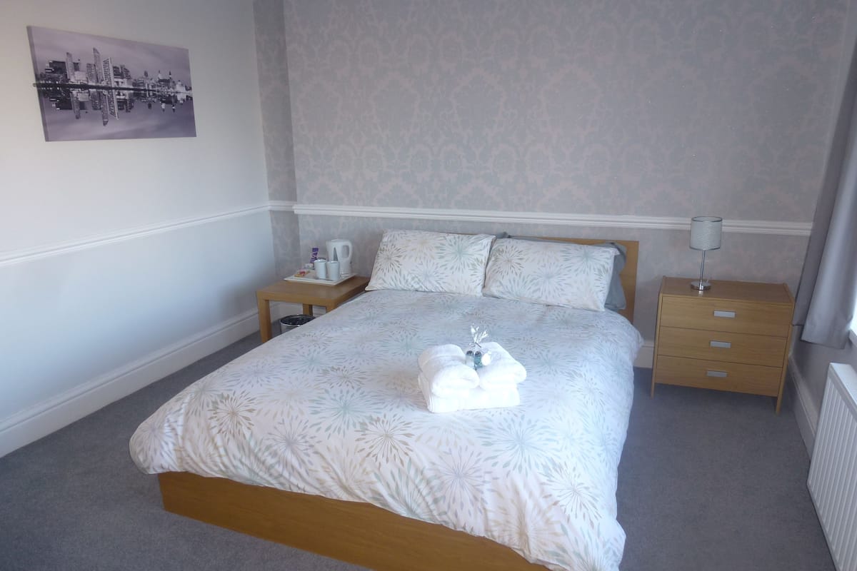 A neatly made bed with a floral bedspread, a bedside table with a lamp, and a wall-mounted picture.