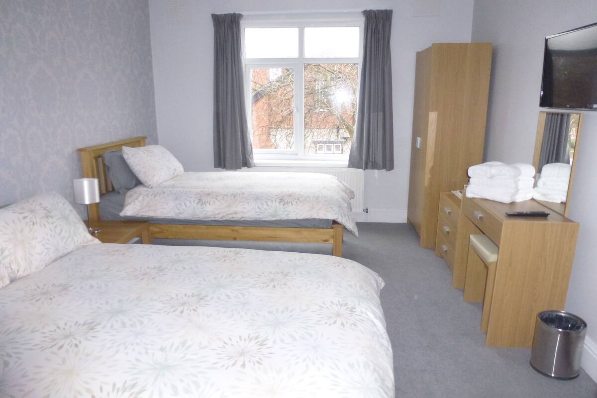 A bedroom with two beds, a wooden wardrobe, a TV, and a window with curtains.