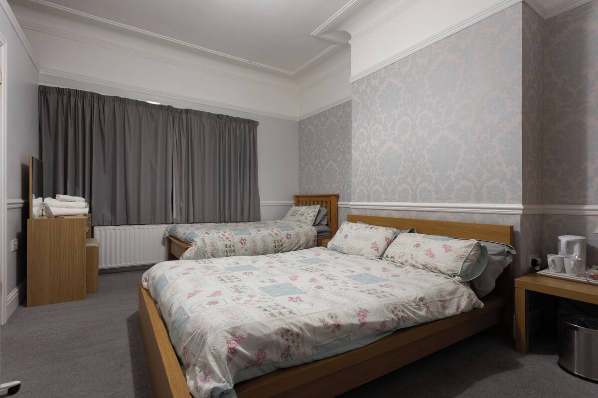 A bedroom with two beds, a wooden dresser, a radiator, and a window with curtains.