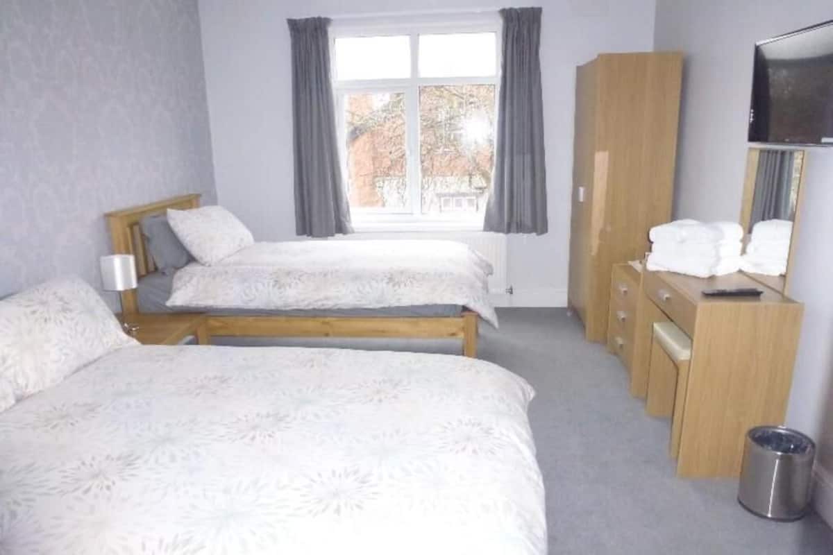 A hotel room with two beds, a wooden wardrobe, a television, and a window with curtains.