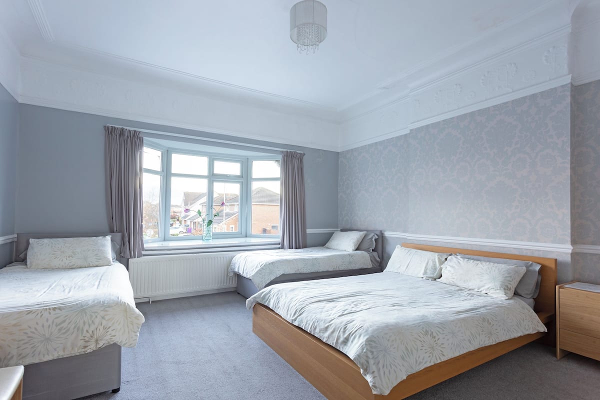 A bedroom with two single beds, a window with curtains, a radiator, and a wooden nightstand.