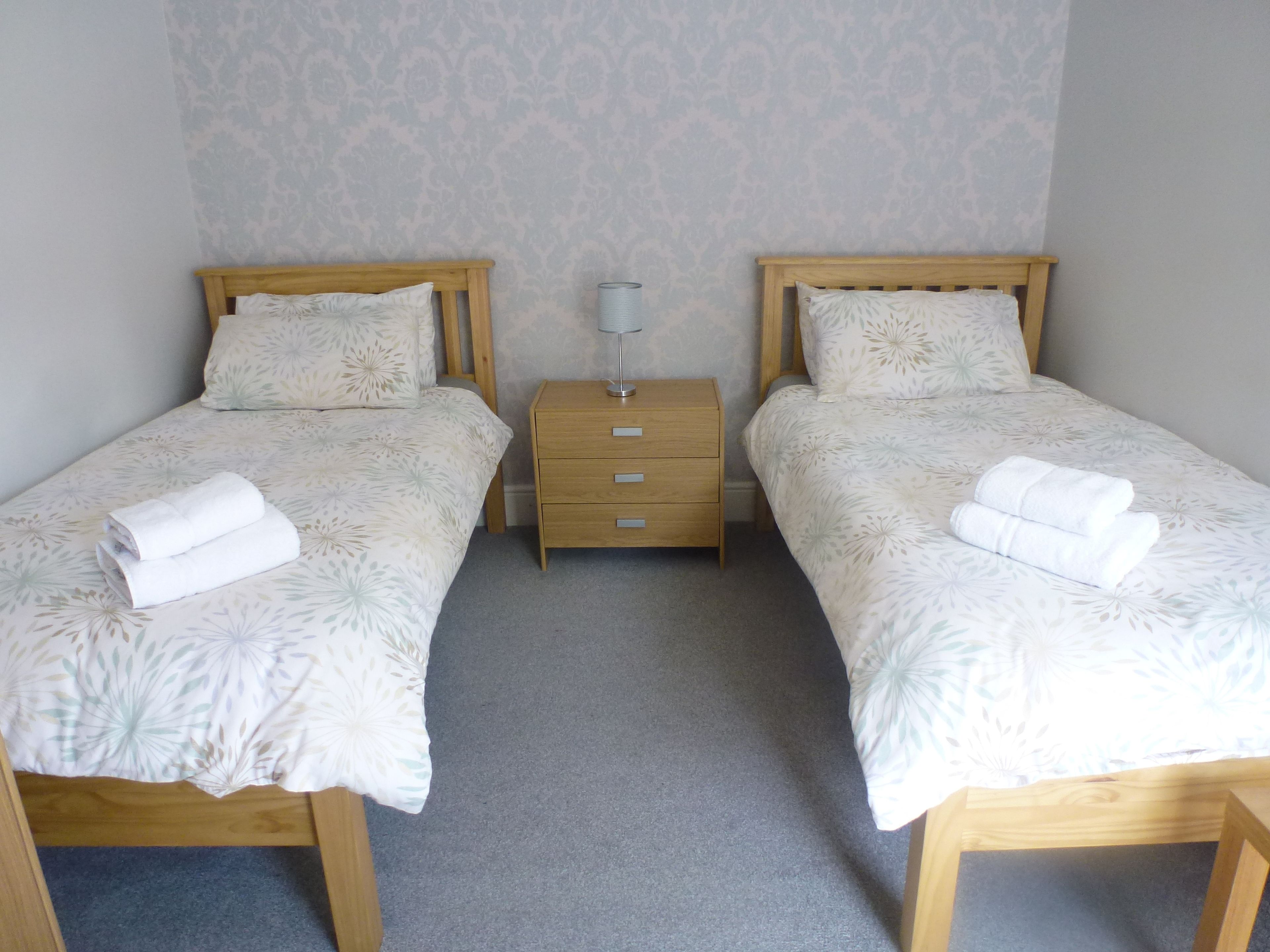 A double room with two single beds, each with a wooden headboard, a small bedside table, and a lamp.
