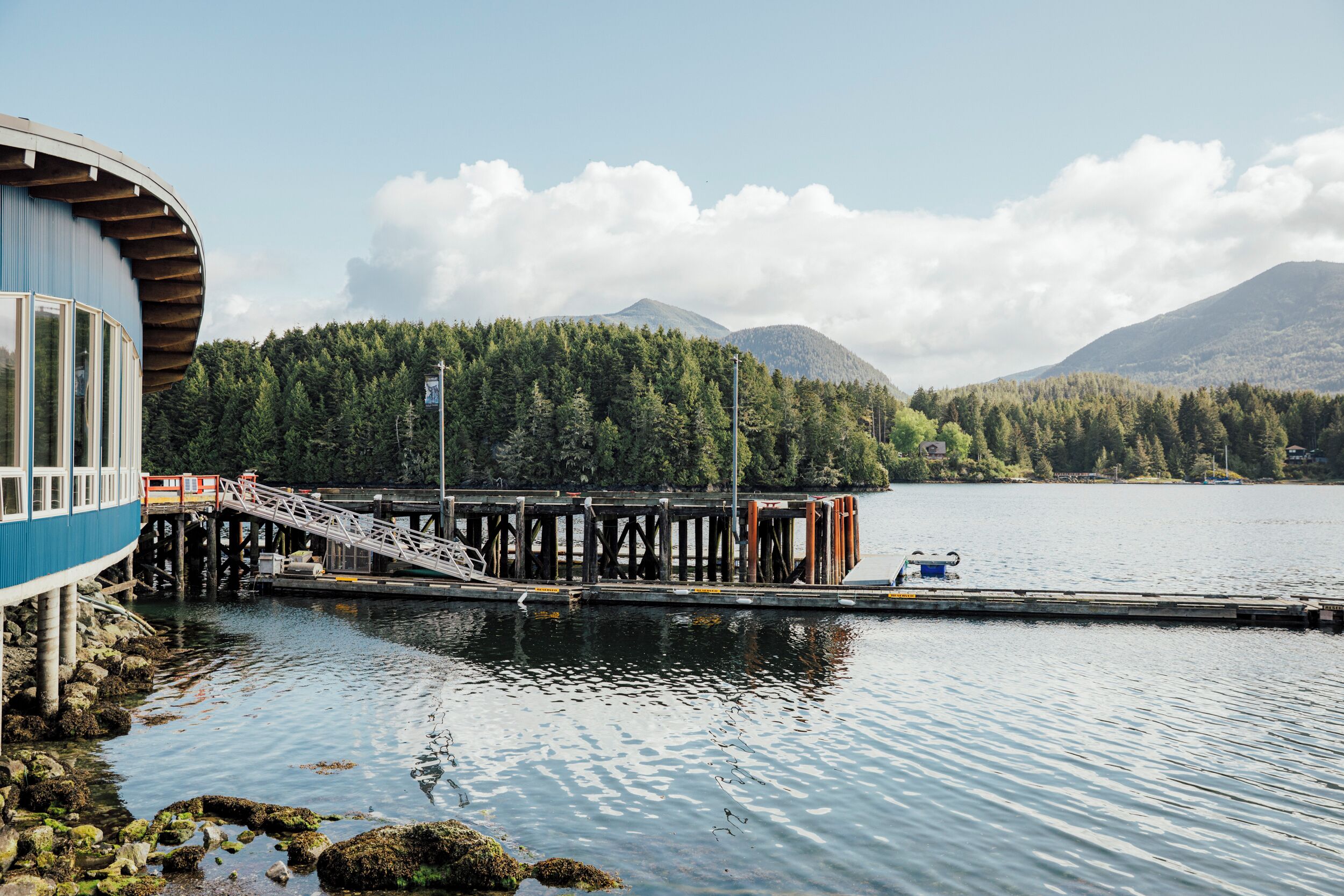 A dock extending into a calm lake with a forested mountain in the background.