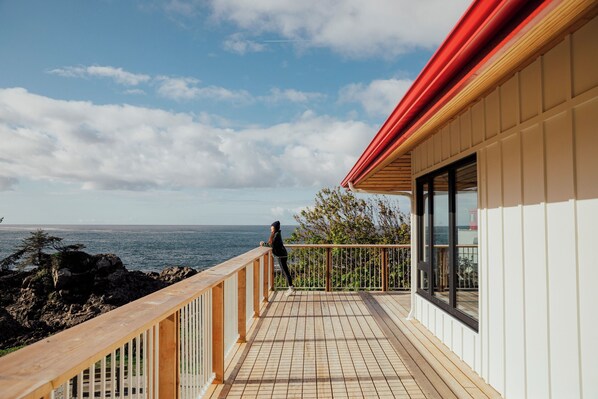 Une terrasse en bois dotée d’une rambarde, qui offre une vue sur une côte rocheuse et la mer.