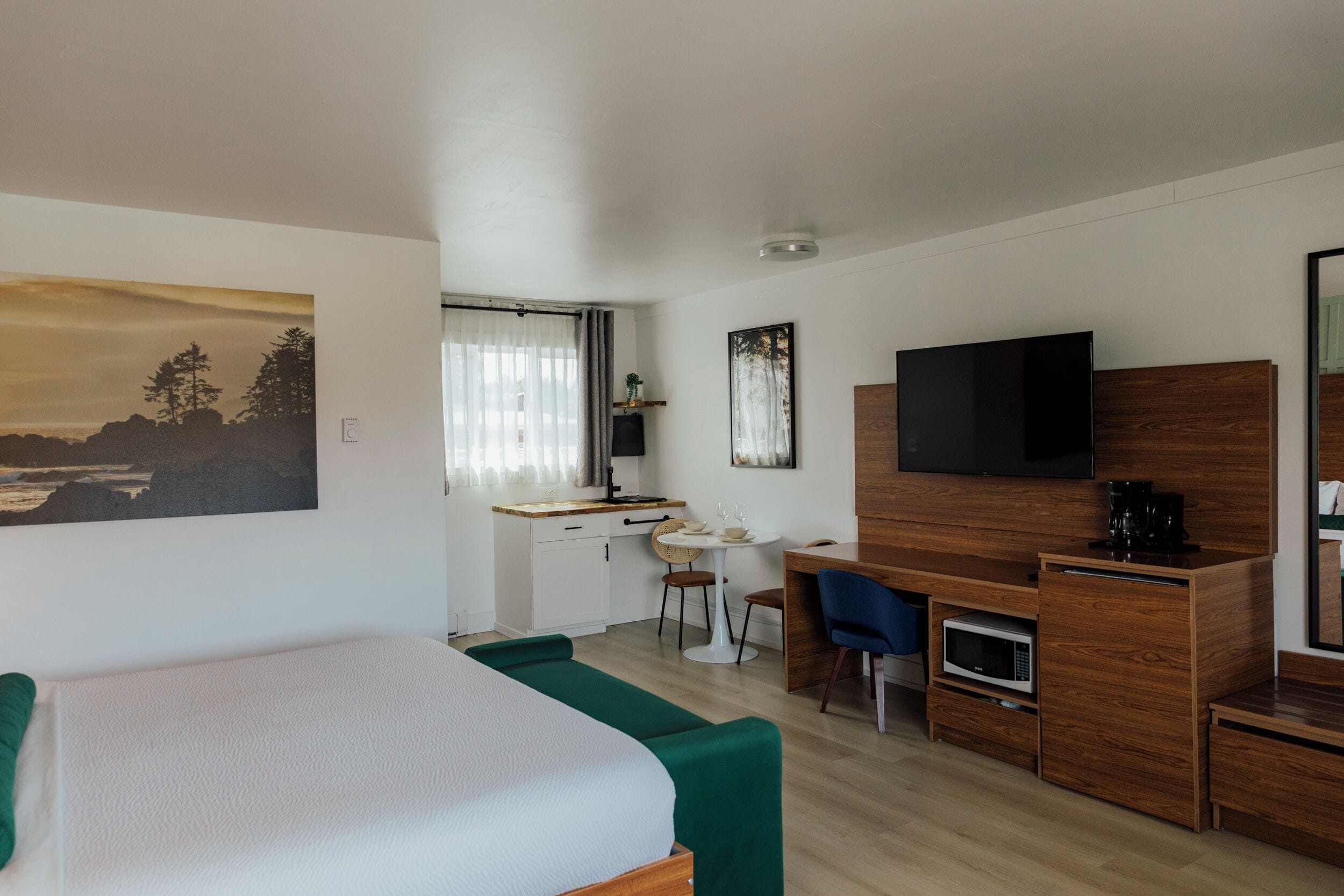 A modern hotel room with a bed, a desk, a television, and a dining area.
