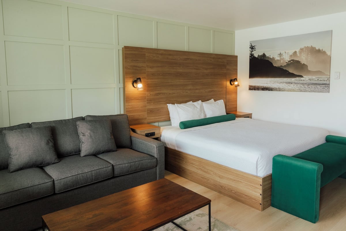 Ein modernes Schlafzimmer mit einem hölzernen Kopfende, einem grauen Sofa, einem Holztisch und einer grünen Bank.
