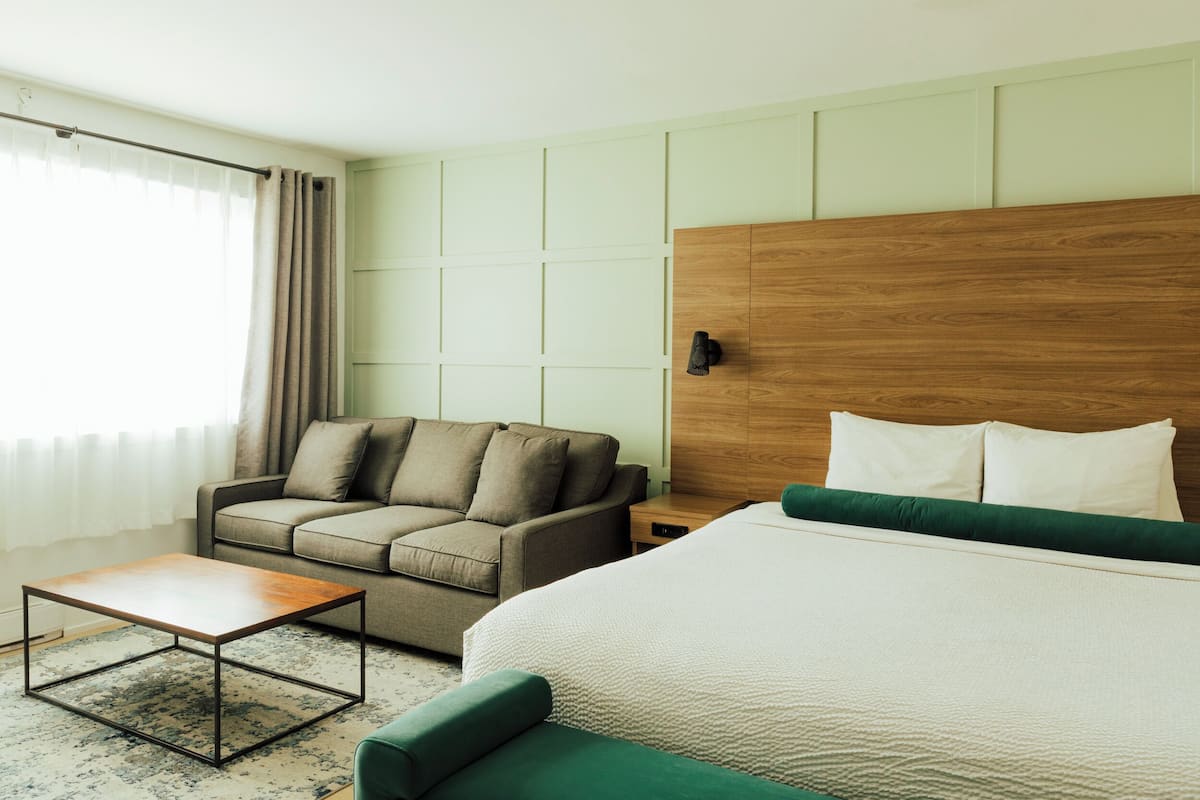 Ein Hotelzimmer mit einem hölzernen Kopfteil, einem grünen Sofa, einem weißen Bett und einem kleinen Tisch.