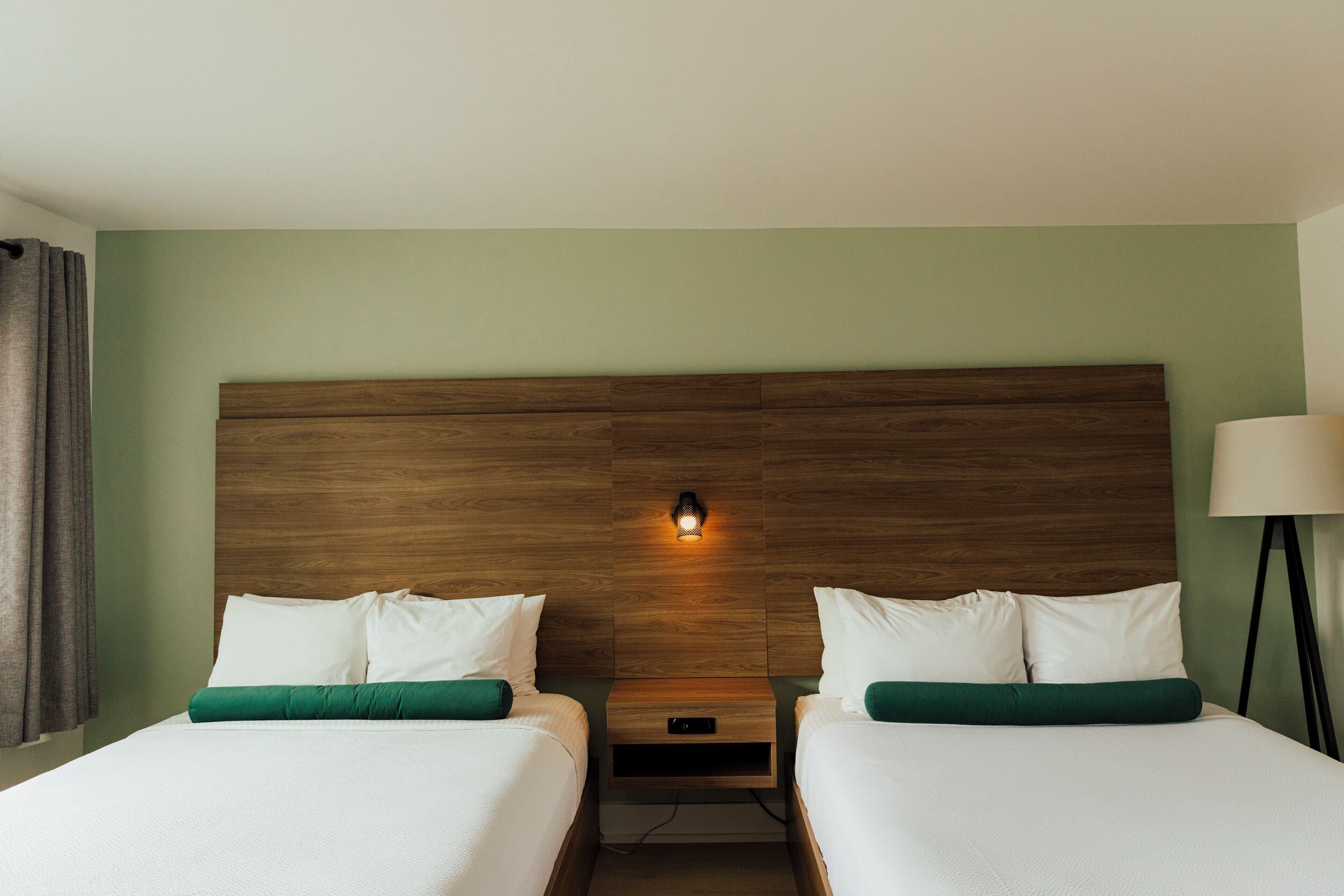 A hotel room with two beds, a wooden headboard, a nightstand, and a lamp.