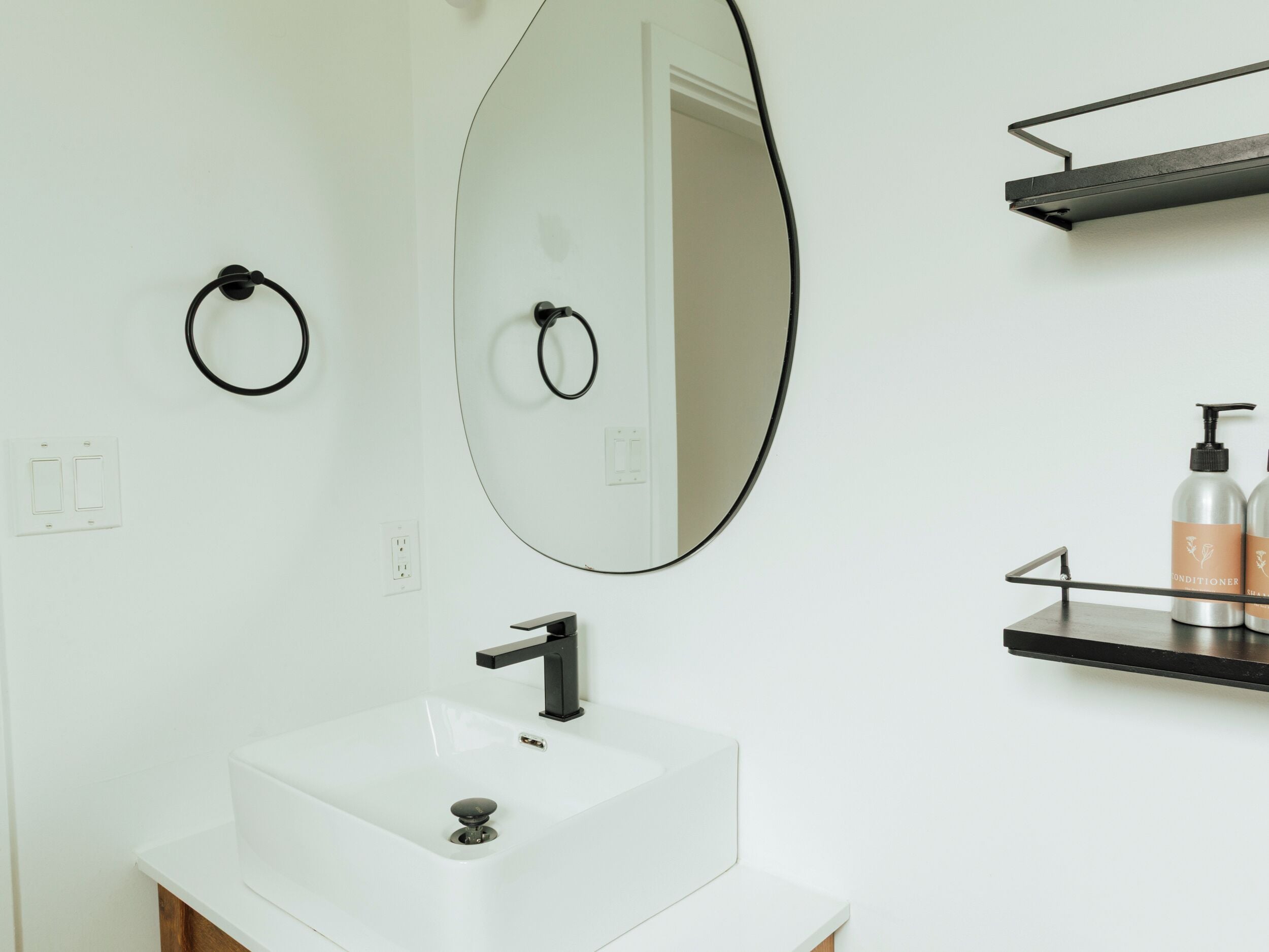 A bathroom with a white sink, a large mirror, and a black towel ring.