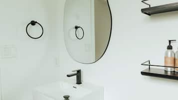 Un baño con un lavamanos blanco, un espejo grande y un tozalengua negro.