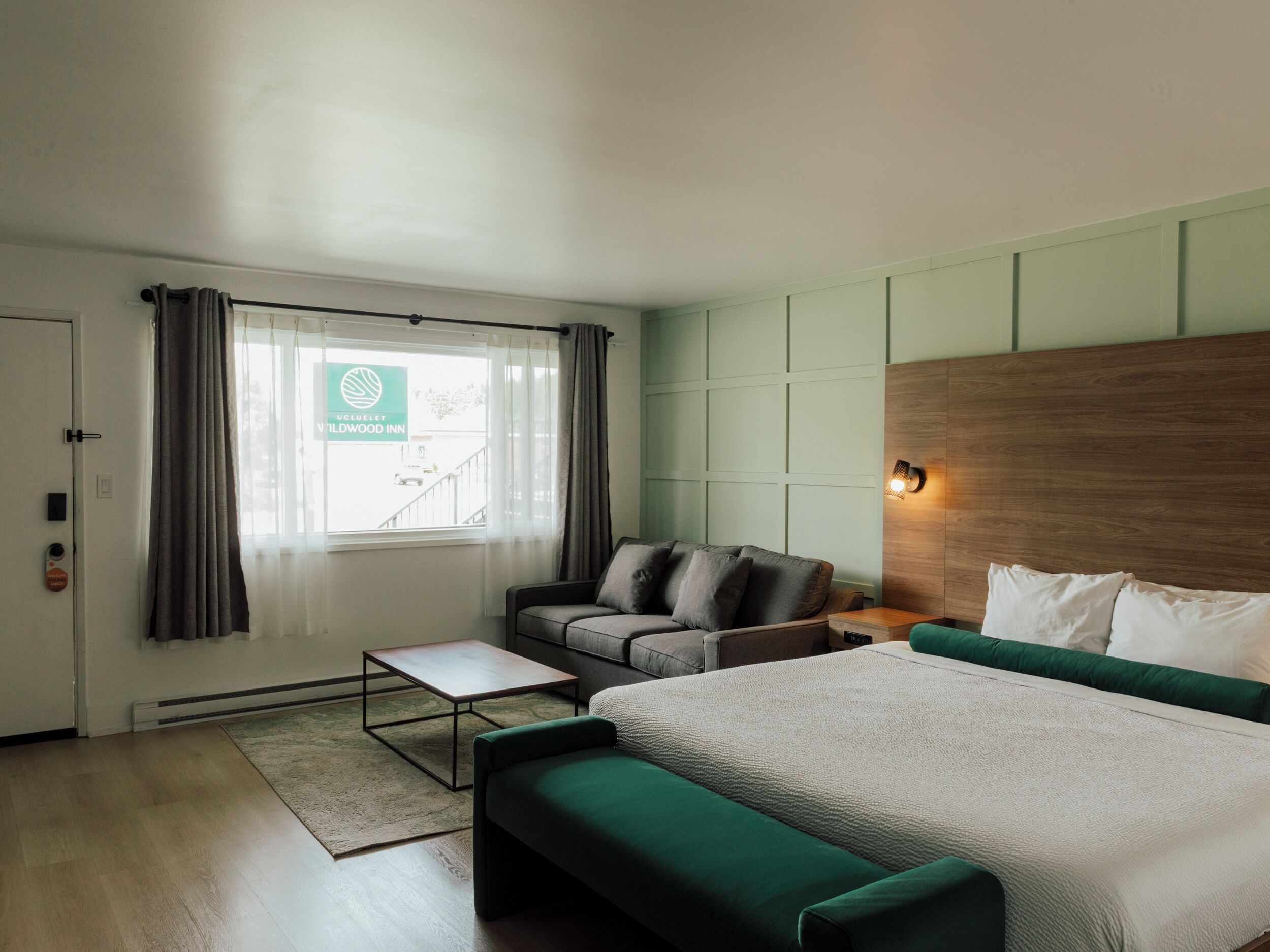 A modern hotel room with a bed, a sofa, a small table, and a view of the outside.