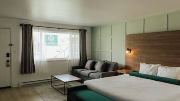 A modern hotel room with a bed, a sofa, a small table, and a view of the outside.