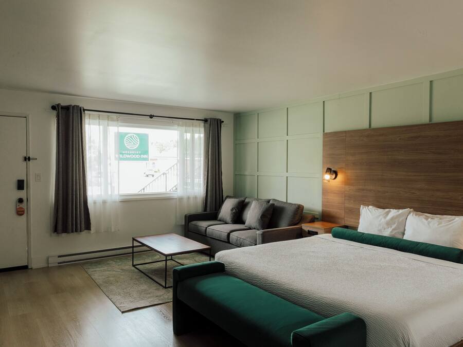 A modern hotel room with a bed, a sofa, a small table, and a view of the outside.